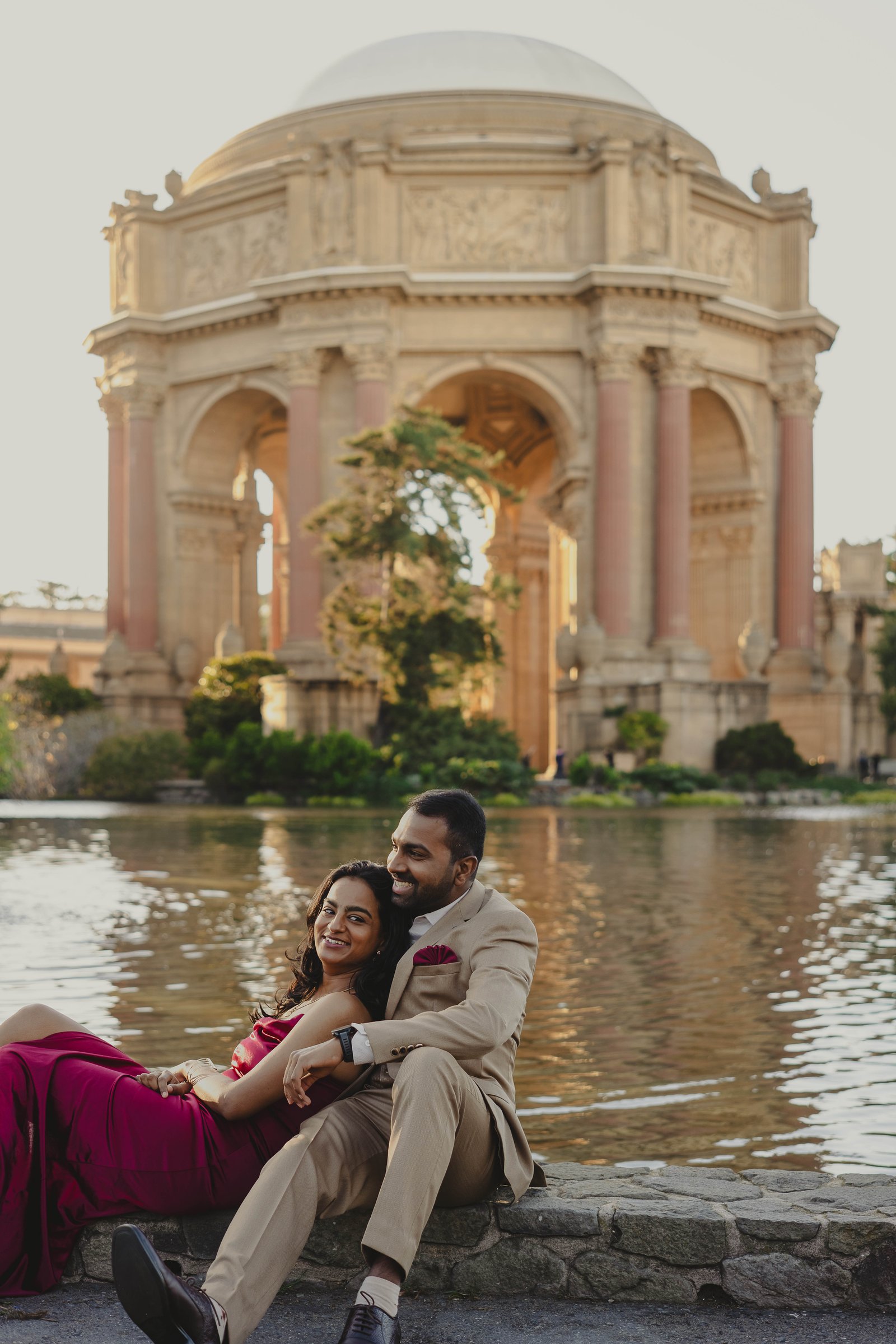 The couple seated by the water with a grand pavilion behind them